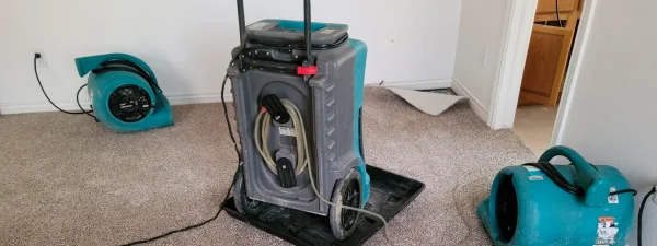 Water damage restoration equipment, including air movers and a dehumidifier, used to dry a carpeted room after a basement flood in Saint Albans, WV.